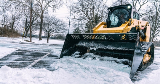 Man operating a Bulldozer to remove snow from a parking lot